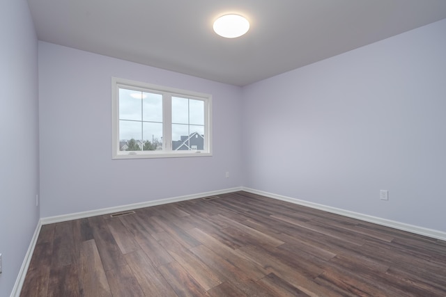 unfurnished room featuring dark wood-type flooring, visible vents, and baseboards