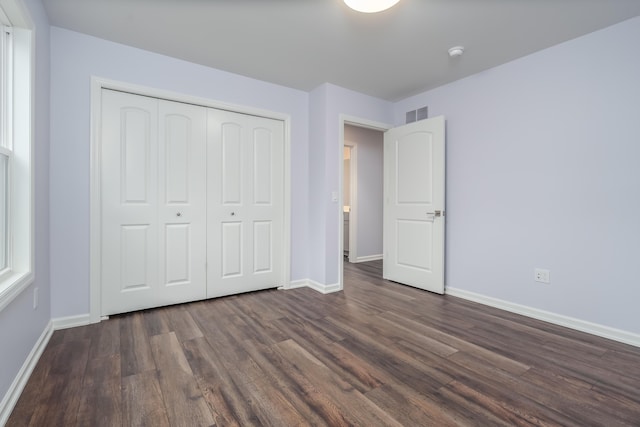 unfurnished bedroom featuring dark wood-style floors, a closet, visible vents, and baseboards