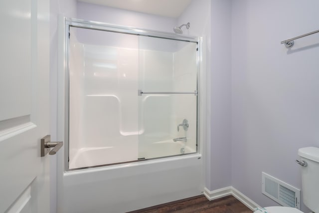 bathroom featuring toilet, bath / shower combo with glass door, wood finished floors, visible vents, and baseboards