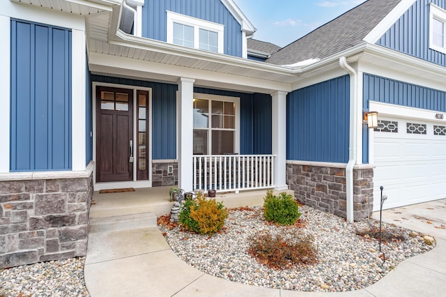 entrance to property featuring stone siding, roof with shingles, an attached garage, covered porch, and board and batten siding