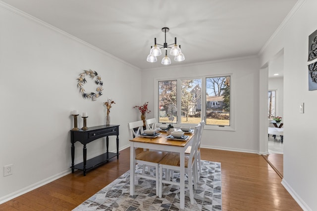 dining space with baseboards, wood-type flooring, a notable chandelier, and ornamental molding