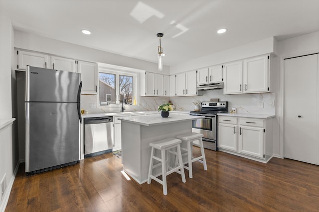 kitchen with dark wood-type flooring, under cabinet range hood, appliances with stainless steel finishes, white cabinetry, and a sink