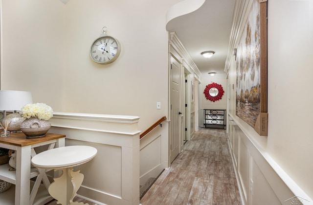 hall with crown molding, a decorative wall, and light wood finished floors