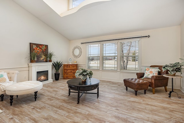 living area featuring wainscoting, lofted ceiling, a glass covered fireplace, light wood-style flooring, and a decorative wall