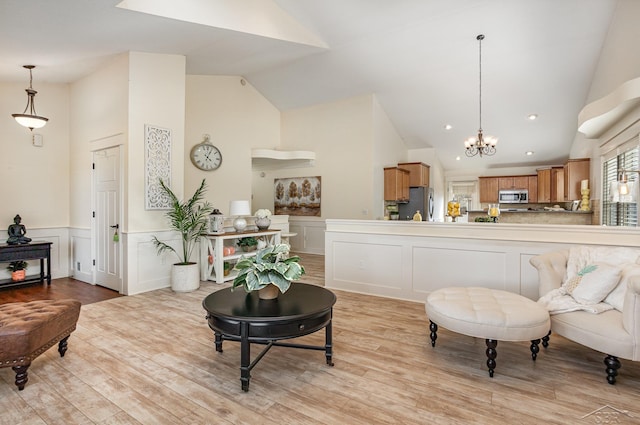 living area featuring lofted ceiling, wainscoting, light wood-style flooring, and an inviting chandelier