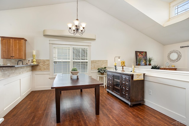 dining area with high vaulted ceiling, dark wood-type flooring, wainscoting, and an inviting chandelier