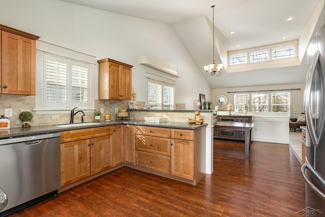 kitchen with dark wood finished floors, a peninsula, stainless steel appliances, a chandelier, and a sink