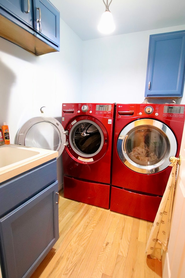 laundry area featuring washer and clothes dryer, cabinet space, and light wood-style flooring