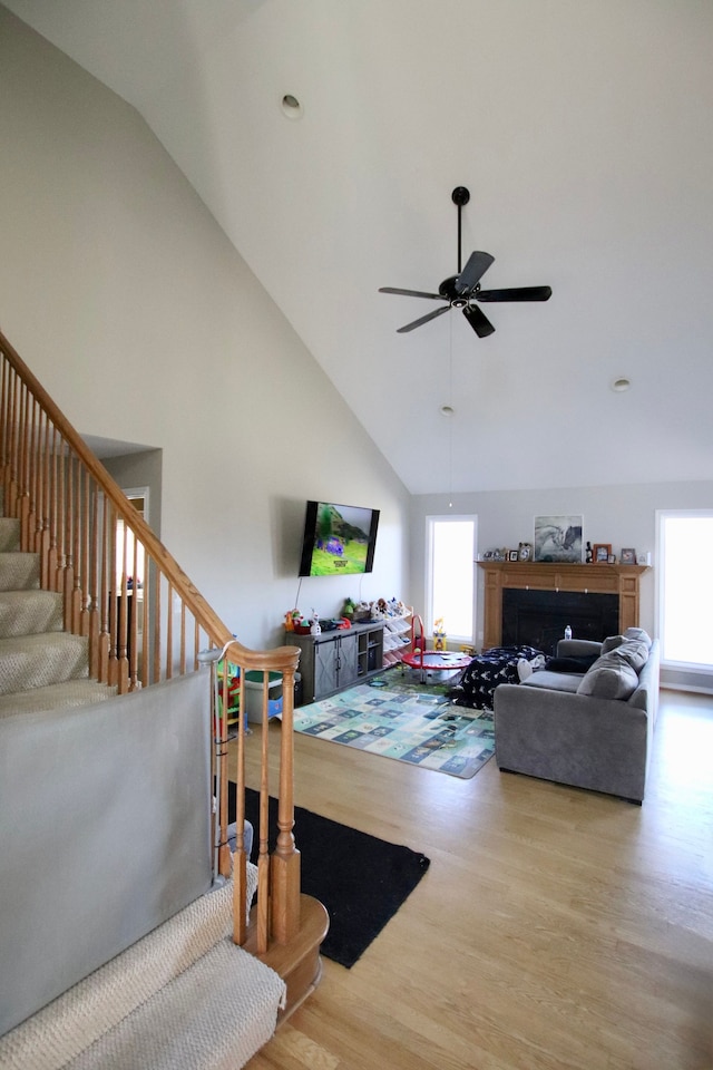 living room featuring stairs, a fireplace, wood finished floors, high vaulted ceiling, and a ceiling fan