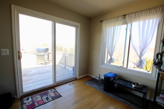 doorway with baseboards, wood finished floors, visible vents, and a healthy amount of sunlight