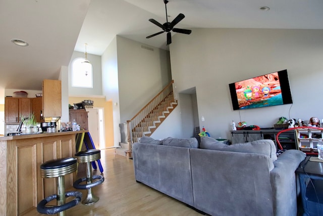 living area with visible vents, light wood-type flooring, stairs, high vaulted ceiling, and a ceiling fan