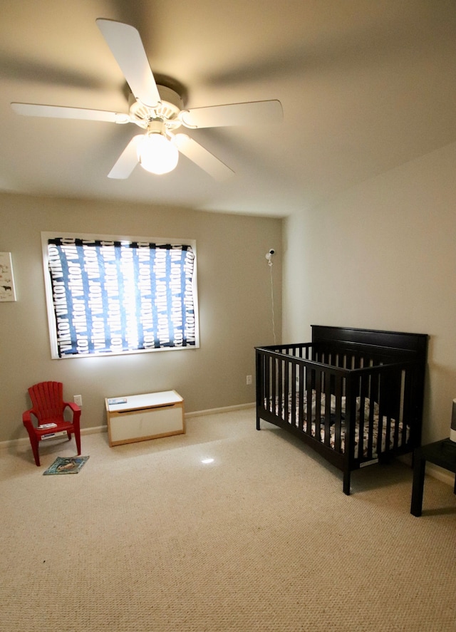 carpeted bedroom featuring a crib, baseboards, and a ceiling fan