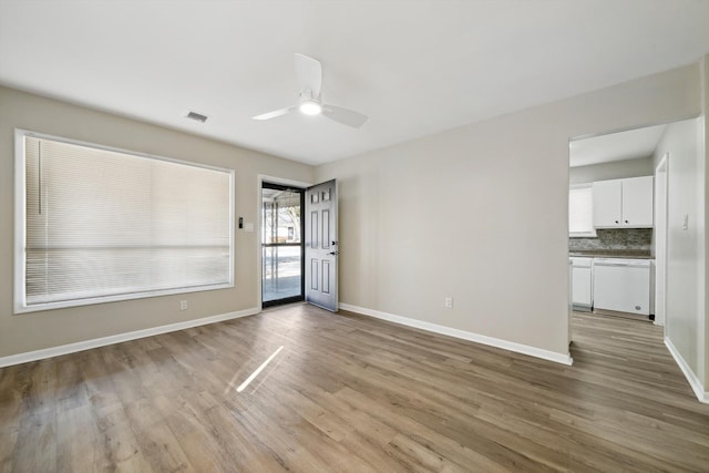 empty room featuring a ceiling fan, wood finished floors, visible vents, and baseboards