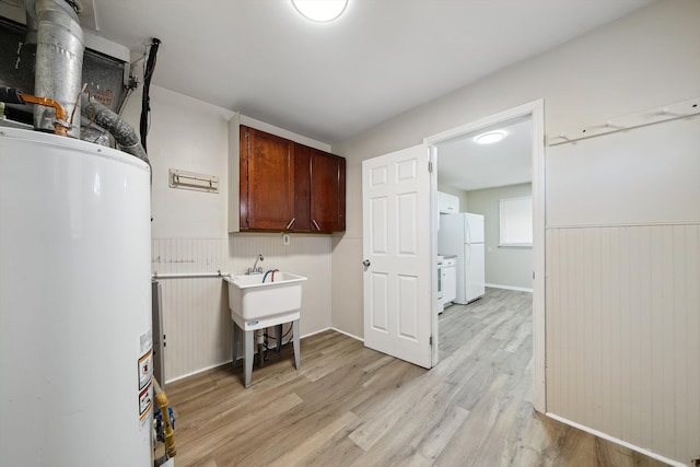 clothes washing area featuring light wood-type flooring, cabinet space, water heater, and wainscoting