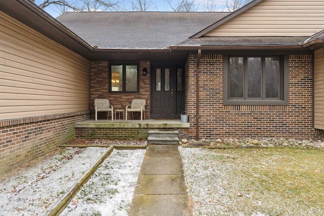 entrance to property with brick siding, a porch, and a shingled roof