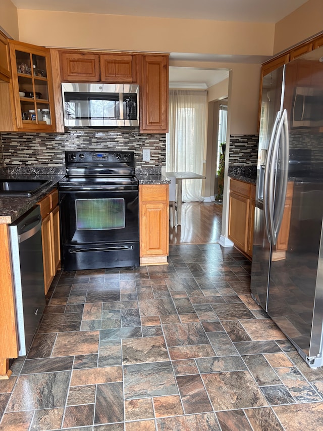 kitchen with dark stone counters, decorative backsplash, glass insert cabinets, appliances with stainless steel finishes, and stone finish flooring