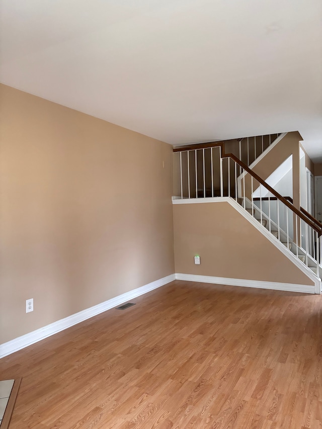 empty room with light wood-type flooring, baseboards, visible vents, and stairway