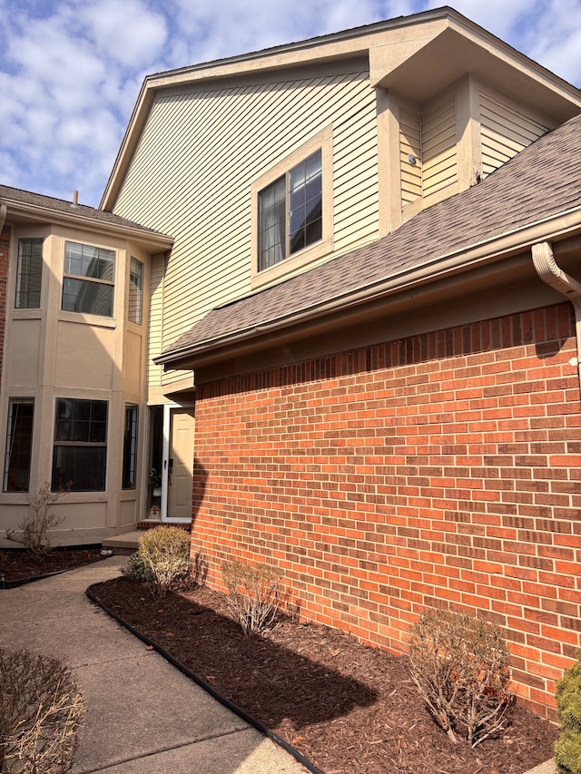 view of property exterior featuring brick siding and a shingled roof