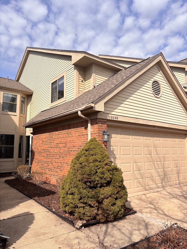 view of front of property featuring brick siding, an attached garage, driveway, and roof with shingles