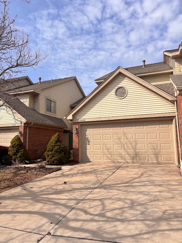 view of front of property featuring a garage, brick siding, concrete driveway, and a shingled roof