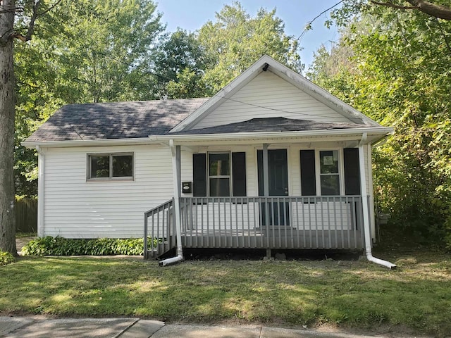 view of front facade featuring a front yard, covered porch, and roof with shingles