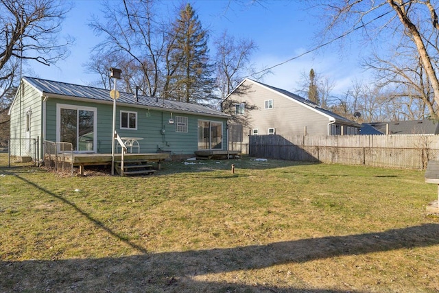 back of property with fence, a wooden deck, a standing seam roof, a lawn, and metal roof