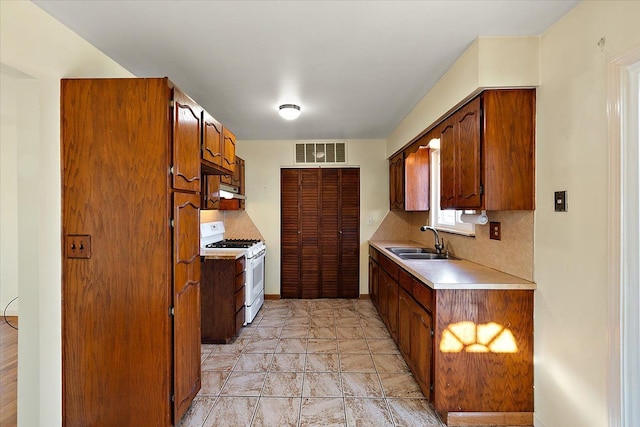 kitchen with brown cabinetry, visible vents, white range with gas cooktop, a sink, and light countertops