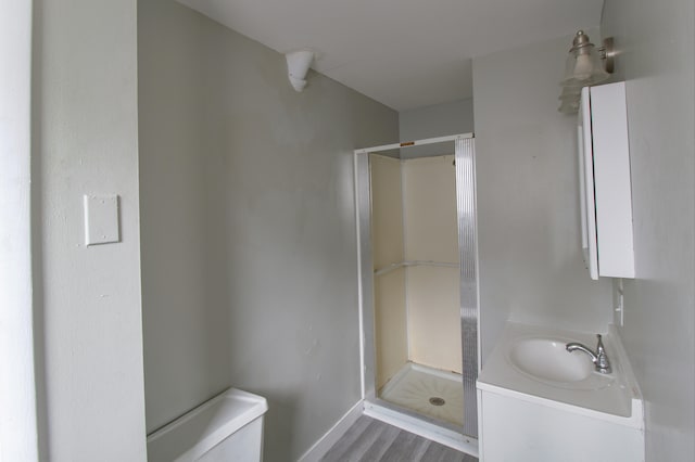 bathroom featuring wood finished floors, a stall shower, vanity, and toilet