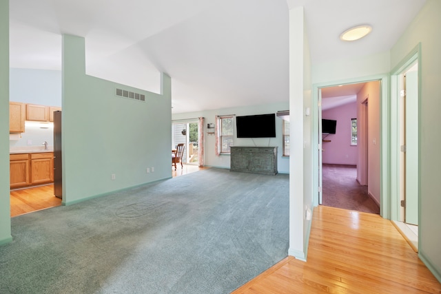 unfurnished living room with lofted ceiling, visible vents, a sink, and light colored carpet