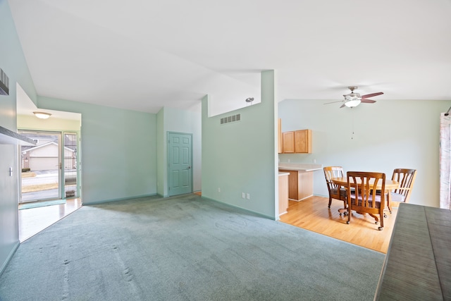 living area with light carpet, visible vents, baseboards, vaulted ceiling, and a ceiling fan