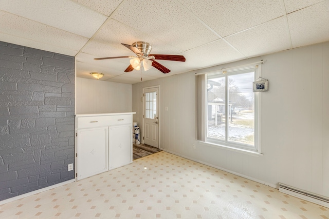 unfurnished room featuring light floors, a ceiling fan, baseboard heating, and a drop ceiling