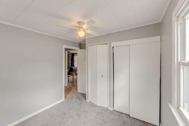 unfurnished bedroom featuring light carpet, baseboards, ceiling fan, ornamental molding, and two closets