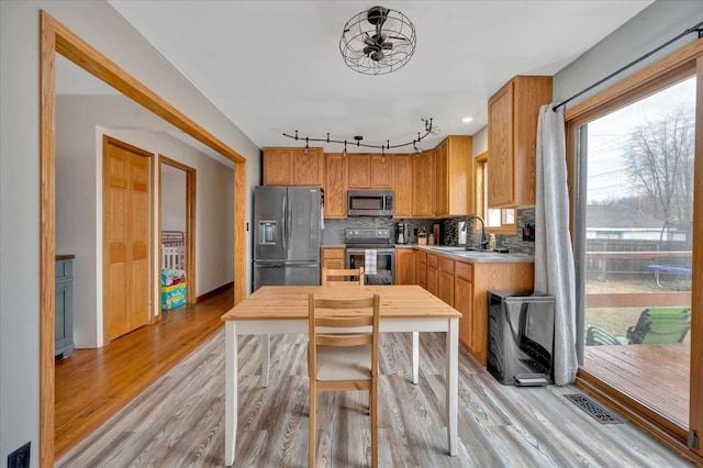 kitchen with a sink, light wood-style floors, light countertops, appliances with stainless steel finishes, and tasteful backsplash