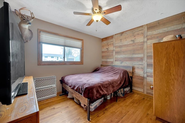 bedroom with a textured ceiling, ceiling fan, wood walls, and light wood-type flooring