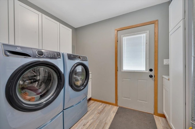 laundry room featuring washer and dryer, cabinet space, light wood-style flooring, and baseboards