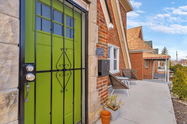 property entrance featuring a porch, brick siding, and a shingled roof