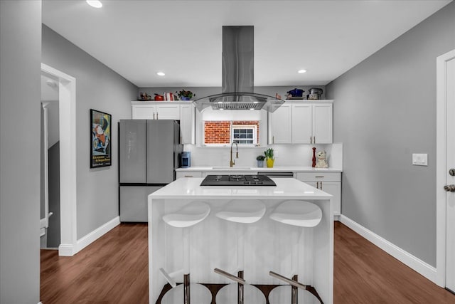 kitchen featuring a breakfast bar area, freestanding refrigerator, light countertops, tasteful backsplash, and island range hood