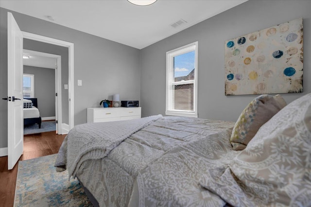 bedroom with visible vents, multiple windows, baseboards, and wood finished floors