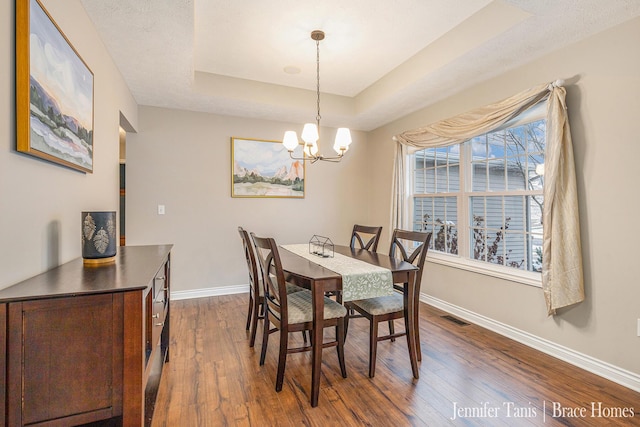 dining area with baseboards, visible vents, a tray ceiling, and dark wood-style flooring