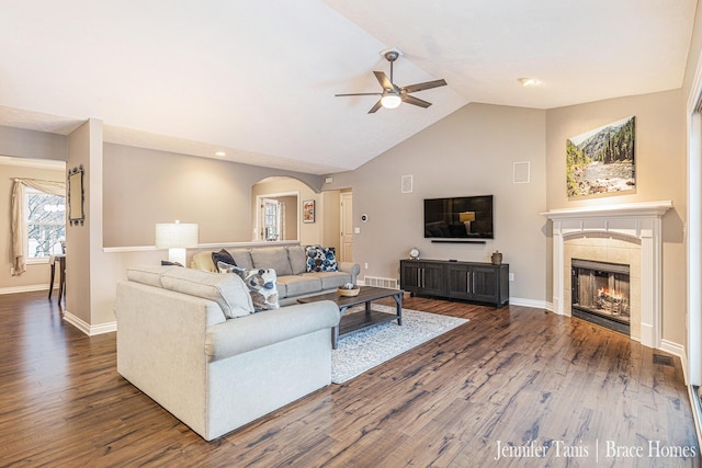 living area with ceiling fan, a tiled fireplace, dark wood finished floors, and baseboards