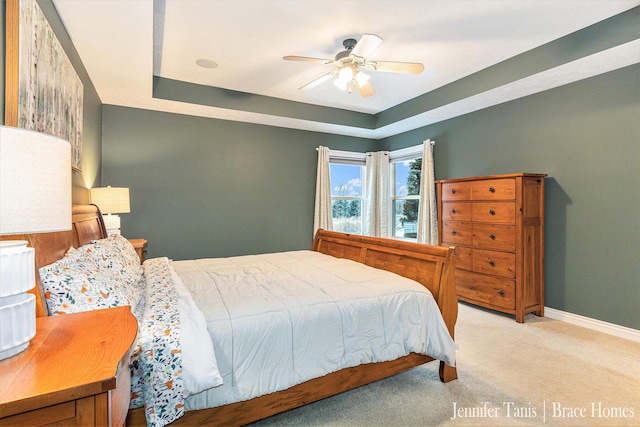 carpeted bedroom with a raised ceiling, a ceiling fan, and baseboards