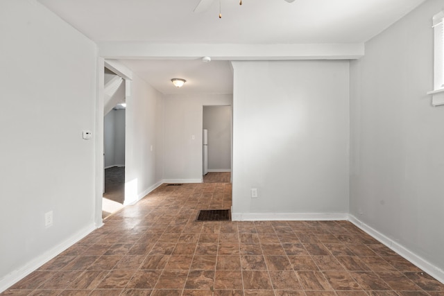 empty room featuring ceiling fan, stone finish floor, visible vents, and baseboards