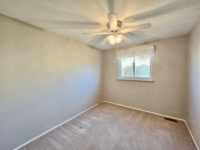 carpeted spare room with visible vents, baseboards, and a ceiling fan