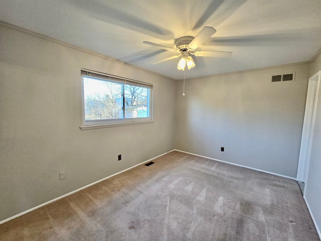 carpeted empty room featuring visible vents, baseboards, ornamental molding, and a ceiling fan