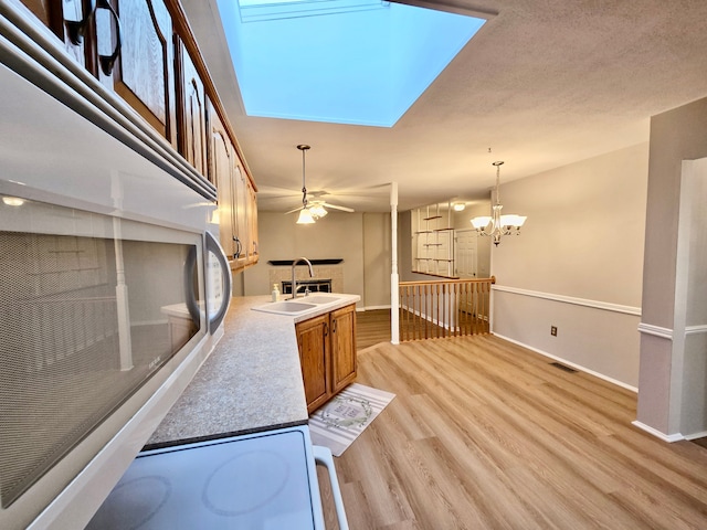 kitchen featuring visible vents, ceiling fan with notable chandelier, a sink, brown cabinetry, and light wood finished floors