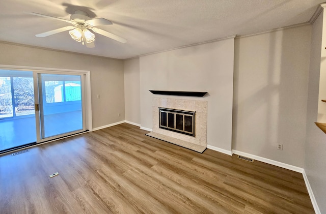 unfurnished living room featuring a tiled fireplace, visible vents, baseboards, and wood finished floors