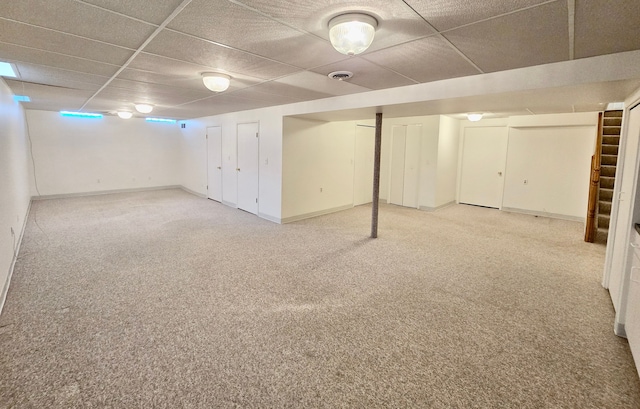 finished below grade area featuring baseboards, a drop ceiling, and light carpet