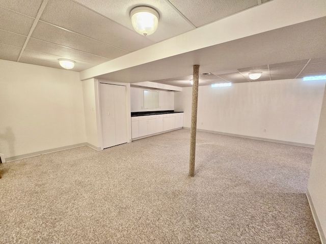 finished below grade area with a paneled ceiling, baseboards, and carpet floors