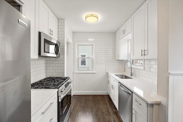 kitchen with dark wood-style flooring, a sink, stainless steel appliances, white cabinetry, and backsplash