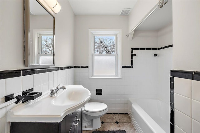 full bath featuring toilet, plenty of natural light, visible vents, and tile walls